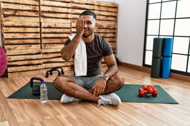 Spor salonundaki antrenman minderinde oturan genç Hintli bir adam bir gözünü eliyle kapatıyor, yüzünde kendine güvenen bir gülümseme ve sürpriz bir duygu var.. 