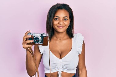 Afro-Amerikalı genç bir kız elinde antika bir kamera tutuyor. Pozitif ve mutlu görünüyor. Kendine güvenen bir gülümsemeyle dişlerini gösteriyor. 