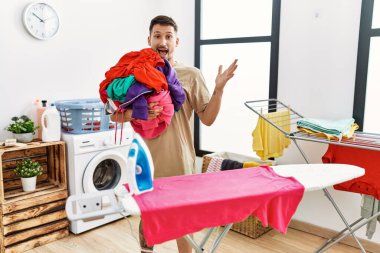 Çamaşırları tutan yakışıklı genç adam zaferi kutlamak için ütülemeye hazır mutlu bir gülümseme ve kaldırılmış ellerle kazanan bir ifadeyle. 