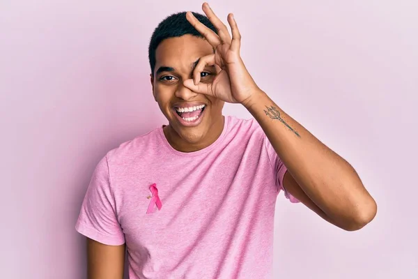 若いですハンサムHispanic男身に着けていますピンク癌リボン上のシャツ笑顔幸せな行いますOk Signとともに手で目を通して指 — ストック写真