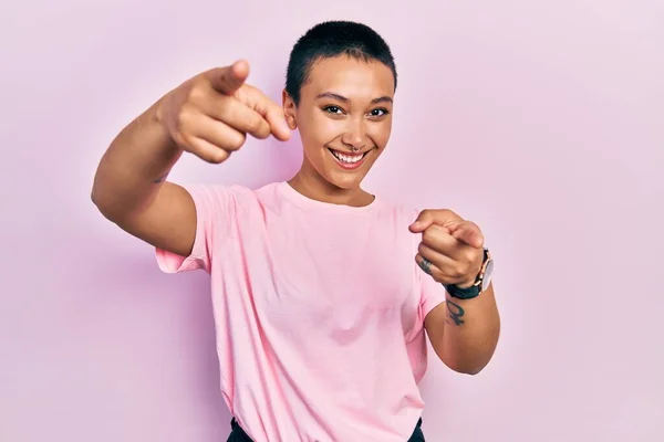 あなたを指すカジュアルなピンクのTシャツを着て短い髪を持つ美しいヒスパニック系の女性と指でカメラ 肯定的で陽気な笑顔 — ストック写真