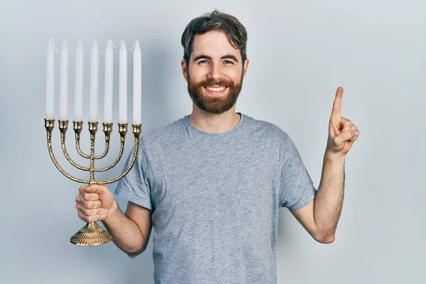 ひげを生やしている白人男性Menora Hanukka Jewishキャンドル笑顔でアイデアや質問を指差す指で幸せな顔 ナンバーワン — ストック写真