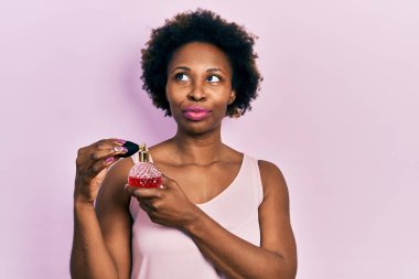 Genç Afrikalı Amerikalı kadın parfüm tutarken gülümsüyor, yan tarafa bakıyor ve düşünüyor.. 