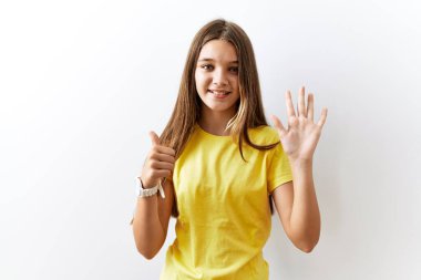 Genç esmer kız izole edilmiş arka planda yan yana duruyor. Altıncı parmaklarıyla işaret ediyor ve gülümsüyor. Kendinden emin ve mutlu.. 