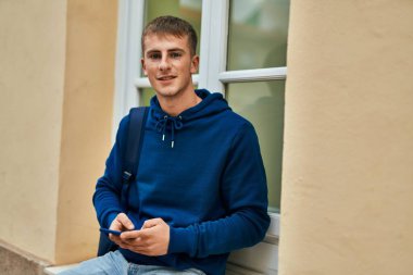 Üniversitede akıllı telefon kullanarak mutlu gülümseyen genç sarışın öğrenci..