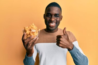 Genç Afro-Amerikalı elinde pişmemiş spagettiyle gülümseyen, mutlu ve pozitif gülümseyen mükemmel ve onay işareti yapan bir adam. 