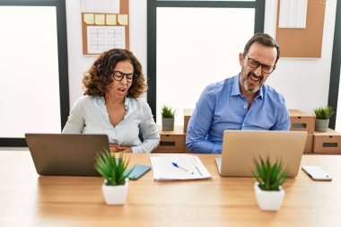 Orta yaşlı İspanyol kadın ve erkek elleri karnında ofiste dizüstü bilgisayarla oturuyorlar çünkü mide bulantısı, acı verici bir hastalık kendini iyi hissetmiyor. Ağrı kavramı. 