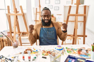 African american artist man at art studio excited for success with arms raised and eyes closed celebrating victory smiling. winner concept. 