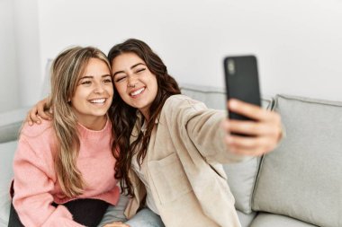 Genç çift mutlu bir şekilde gülümsüyor. Evdeki akıllı telefonun yanında selfie çekiyorlar..
