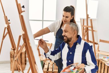 Genç resim öğretmeni kadın sanat stüdyosundaki tuvalde resim yapan yaşlı adama resim öğretiyor.