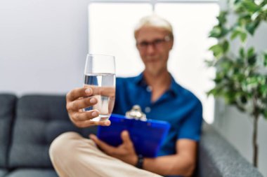 Psikolog terapisi yapan genç beyaz bir adam psikoloji kliniğinde su bardağı tutuyor.