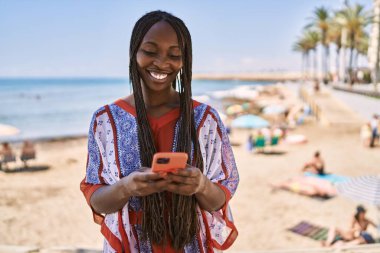 Genç Afrikalı Amerikalı kadın sahilde akıllı telefon kullanıyor..