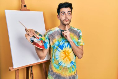 İspanyol asıllı genç bir adam paletle resim çiziyor. Resim sehpası ayakta durup şüphe üzerine kafa yoruyor. Parmakları çenesinde ve yukarı bakıyor. 