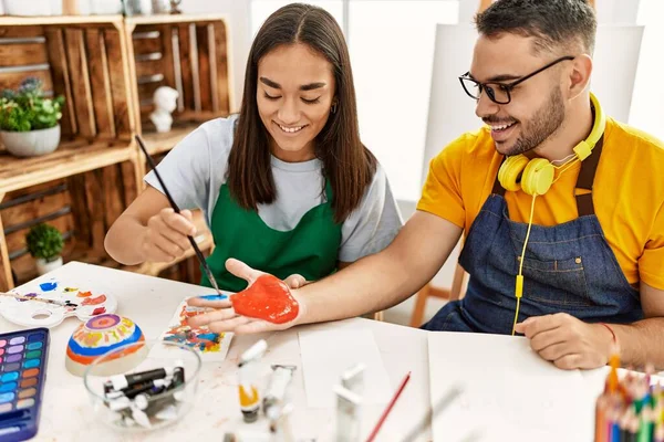 stock image Young hispanic couple smiling happy painting hands sitting on the table at art studio.