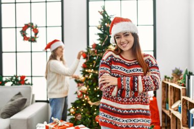 Evdeki güzel çift Noel ağacının yanında durmuş kollarını kavuşturup kameraya bakarken gülümsüyor. pozitif kişi. 
