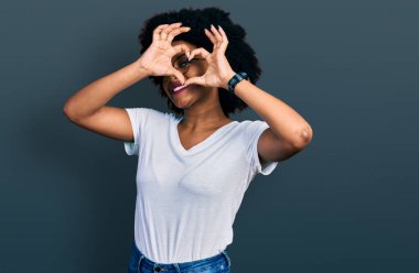 Genç Afro-Amerikalı kadın, günlük beyaz tişörtler giyip kalp şeklinde el ve parmaklarıyla tabelanın içinden bakıp gülümsüyor. 
