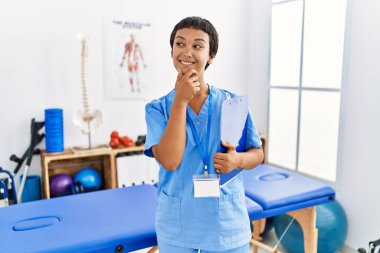 Kısa saçlı, İspanyol bir kadın ağrı kesici kliniğinde çalışıyor. Kameraya bakıyor. Kollarını kavuşturup, çenesini kaldırarak gülümsüyor. Olumlu düşünmek. 