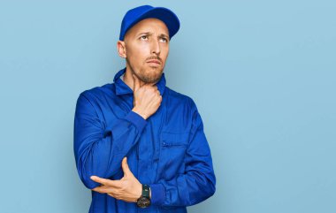 Kel, sakallı, işçi tulumu giyen, boynu ağrıyan, grip, mantar ve enfeksiyon yüzünden boğaz ağrıyan bir adam. 