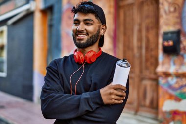 Genç Arap adam gülümsüyor. Elinde grafiti spreyi tutuyor.