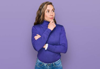 Elleri çenesinde gündelik giysiler giymiş soru soran genç sarışın kadın, düşünceli bir ifade. Düşünceli bir yüzle gülümsüyor. şüphe kavramı. 