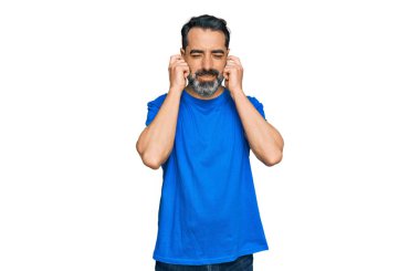 Orta yaşlı, sakallı, günlük mavi tişörtlü, kulaklarını parmaklarıyla kapatan yüksek sesli müzik sesi için rahatsız edici ifadeler takınan bir adam. sağır kavramı. 