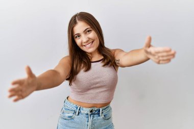 Genç esmer kadın, izole edilmiş arka planda durup kameraya bakarak sarılmak için kollarını açmış gülümsüyor. Mutluluğu kucaklayan neşeli bir ifade.. 