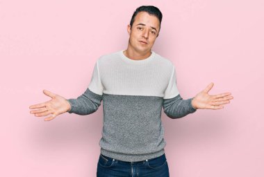 Sıradan bir kazak giyen yakışıklı ve elleri ve kolları havada, kafası karışık genç bir adam. şüphe kavramı. 