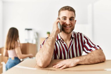 Genç İspanyol adam akıllı telefondan konuşuyor. Yeni evde karton üzerine yaslanıyor..