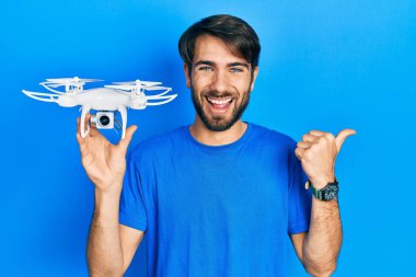 Genç İspanyol bir adam İHA 'yı elinde tutuyor başparmağıyla yan tarafa bakıyor mutlu bir şekilde ağzı açık gülümsüyor. 