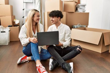 Genç ve güzel çift yeni evlerinde dizüstü bilgisayar kullanarak mutlu bir şekilde gülümsüyor..