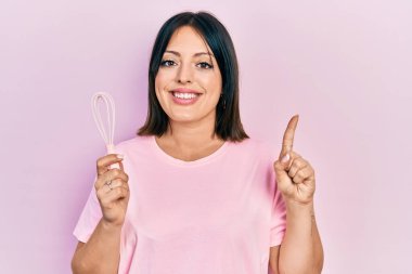 Genç İspanyol kadın fırça kullanarak yemek pişiriyor. Bir fikir veya soruyla gülümsüyor. Mutlu bir yüzle işaret ediyor. 