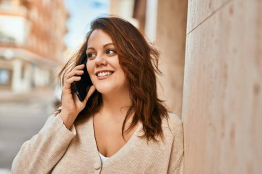 Genç İrlandalı artı cüsseli kız gülümseyerek şehirde akıllı telefondan konuşmaktan mutlu oluyor..