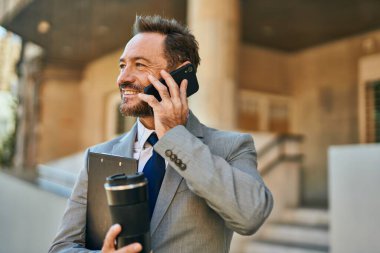 Orta yaşlı işadamı akıllı telefondan konuşuyor ve şehirde kahve içiyor..