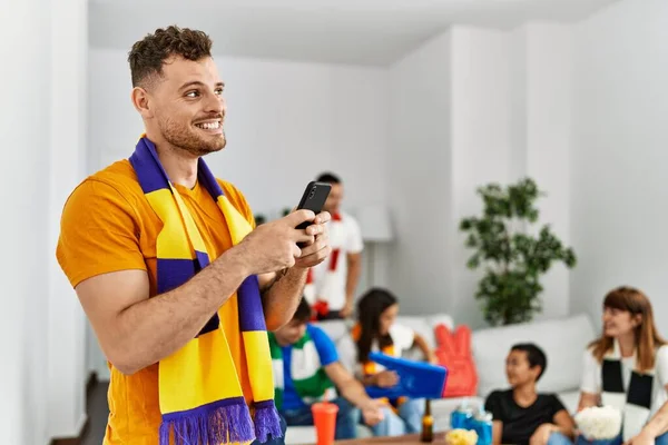 サッカーの試合を見て支援する若い友人のグループ 家でスマホを使って笑顔を見せる男 — ストック写真