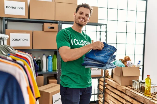 Ung Latinamerikan Man Bär Volontär Uniform Håller Hopfällda Jeans Välgörenhetscenter — Stockfoto