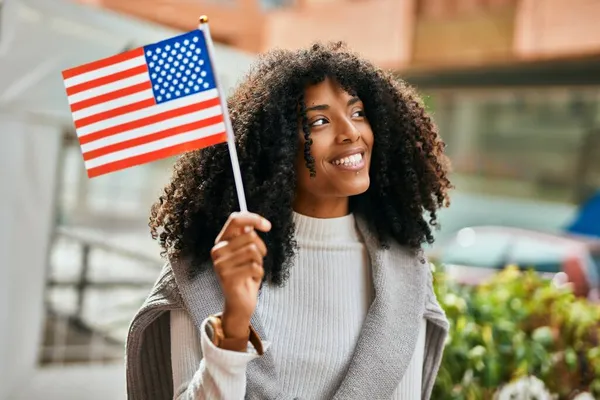 Young african american woman smiling happy holding United States flag at the city.