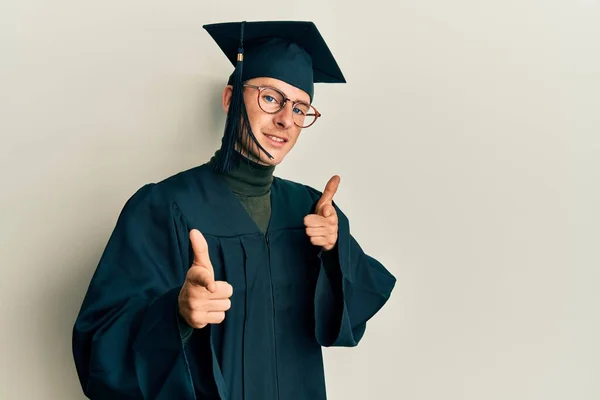 卒業キャップと儀式用のローブを身に着けている若い白人男性は 幸せで面白い顔でカメラに指を指しています 良いエネルギーと振動は — ストック写真
