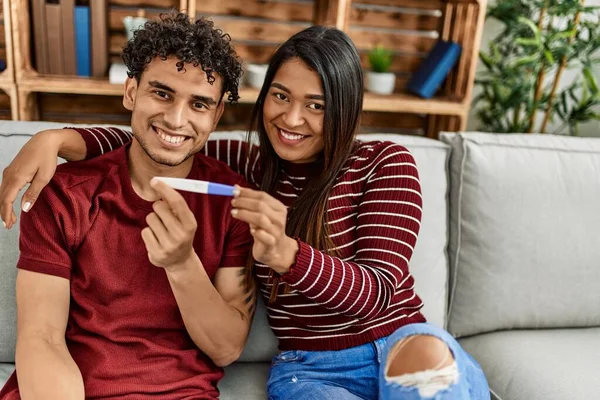 Młoda Latynoska Para Uśmiechnięta Szczęśliwy Trzymając Test Ciążowy Siedzi Kanapie — Zdjęcie stockowe