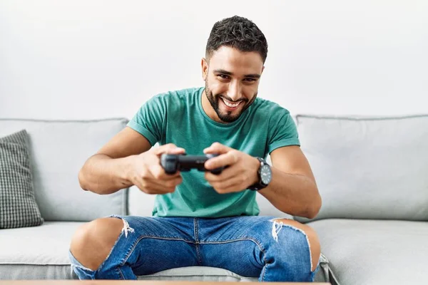 年轻的阿拉伯男子坐在家里的沙发上玩电子游戏 — 图库照片
