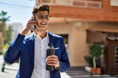 Akıllı telefondan konuşan genç adam sokakta takım elbise ve gözlük takıyor.