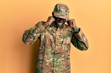 Genç Afro-Amerikan üniformalı adam yüksek sesli müzik sesi için kulaklarını parmaklarıyla kapatıyor. sağır kavramı. 