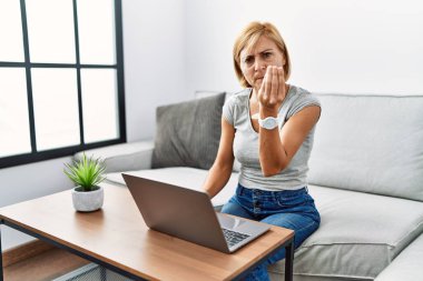 Orta yaşlı sarışın kadın evinde dizüstü bilgisayar kullanıyor. İtalyan jestleri yapıyor. Elleri ve parmakları kendine güveni tam. 