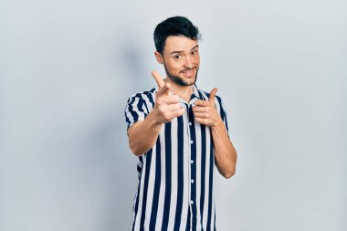 Günlük kıyafetler giyen genç İspanyol adam mutlu ve komik yüzüyle kamerayı işaret ediyor. iyi enerji ve titreşimler. 