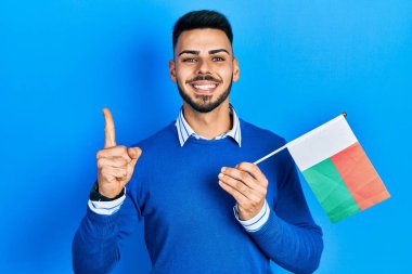 Sakallı, elinde madagaskar bayrağı olan genç İspanyol bir adam bir fikir veya soruyla gülümsüyor. 