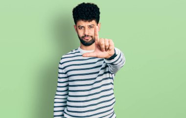 Sakallı, sıradan çizgili süveter giyen genç bir Arap parmağını kaldırmış ve kızgın bir ifade takınıyor. 