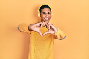 Genç Afro-Amerikalı adam kulaklıkla müzik dinliyor. Aşkta gülümsüyor. Elleriyle kalp sembolü yapıyor. romantik kavram. 