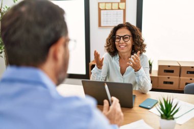 İki orta yaşlı iş adamı ofiste konuşurken gülümsüyor..