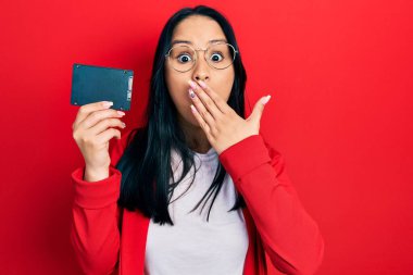 Burnunda piercing olan güzel bir İspanyol kadın ağzını eliyle kapatan SSD hafızası taşıyor, şok geçiriyor ve hata yapmaktan korkuyor. şaşırmış ifade 