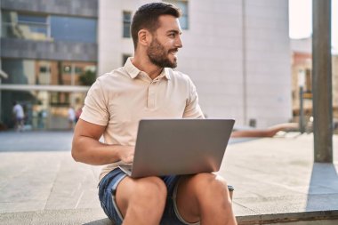 Sokakta dizüstü bilgisayar kullanarak gülümseyen İspanyol genç adam.
