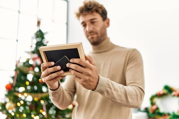 Joven Hispano Sosteniendo Foto Pie Junto Árbol Navidad Casa —  Fotos de Stock